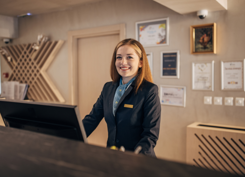 Uśmiechnięta pracownica hotelowej recepcji za ladą.